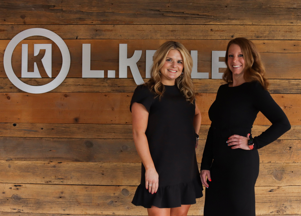Two women standing in front of a sign that says l.k.le