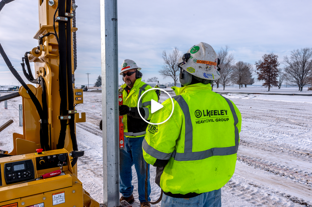 Two construction workers are working on a pole in the snow.