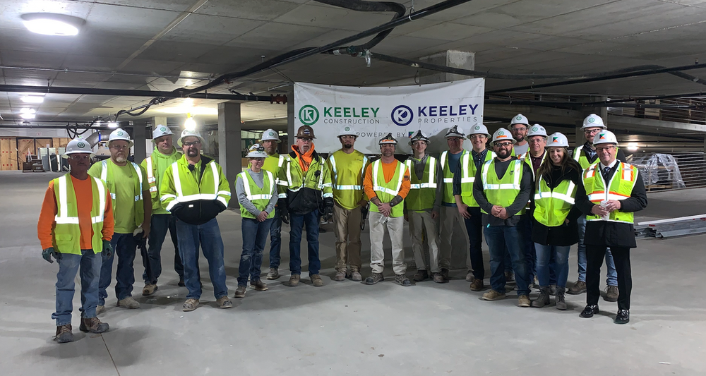A group of construction workers are posing for a picture in a parking garage.