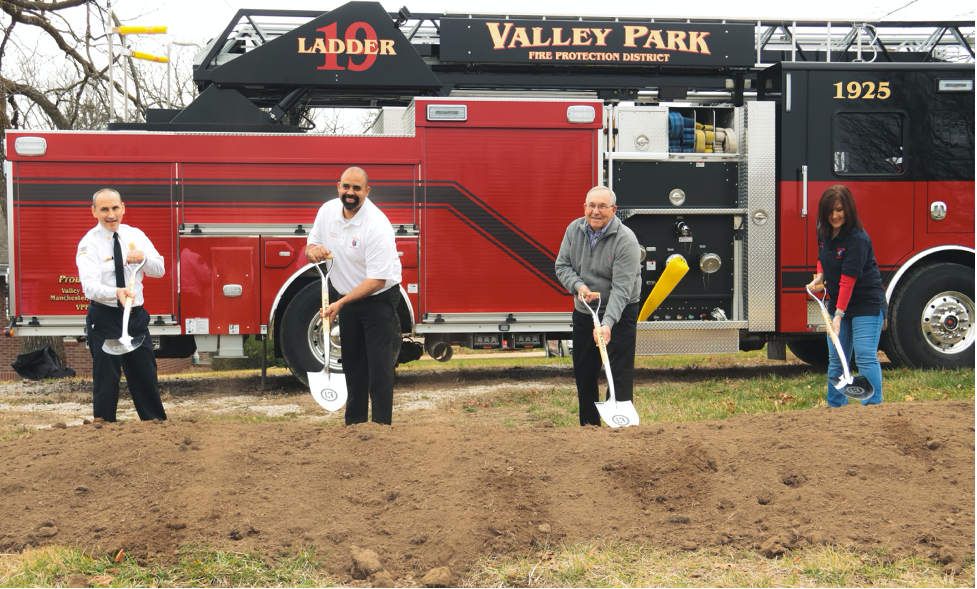 A group of people shoveling dirt in front of a valley park fire truck