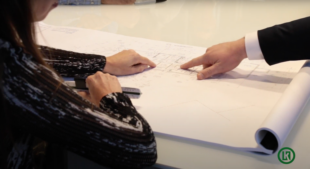 A man and a woman are sitting at a table looking at a blueprint.
