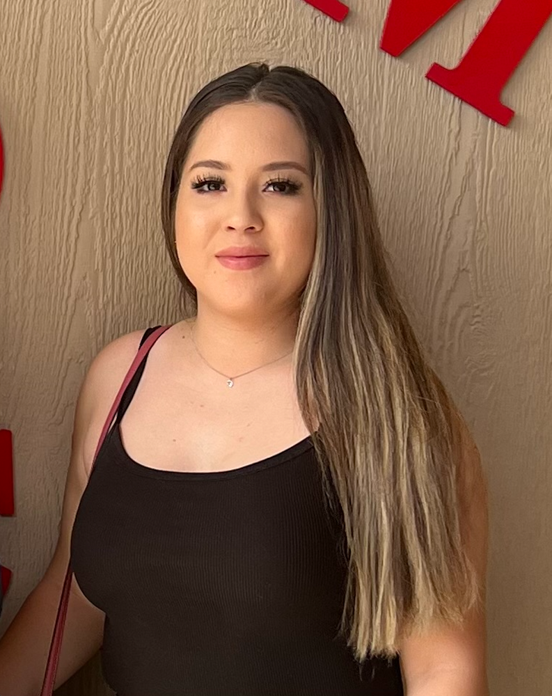A woman in a black tank top is standing in front of a wall with red letters.