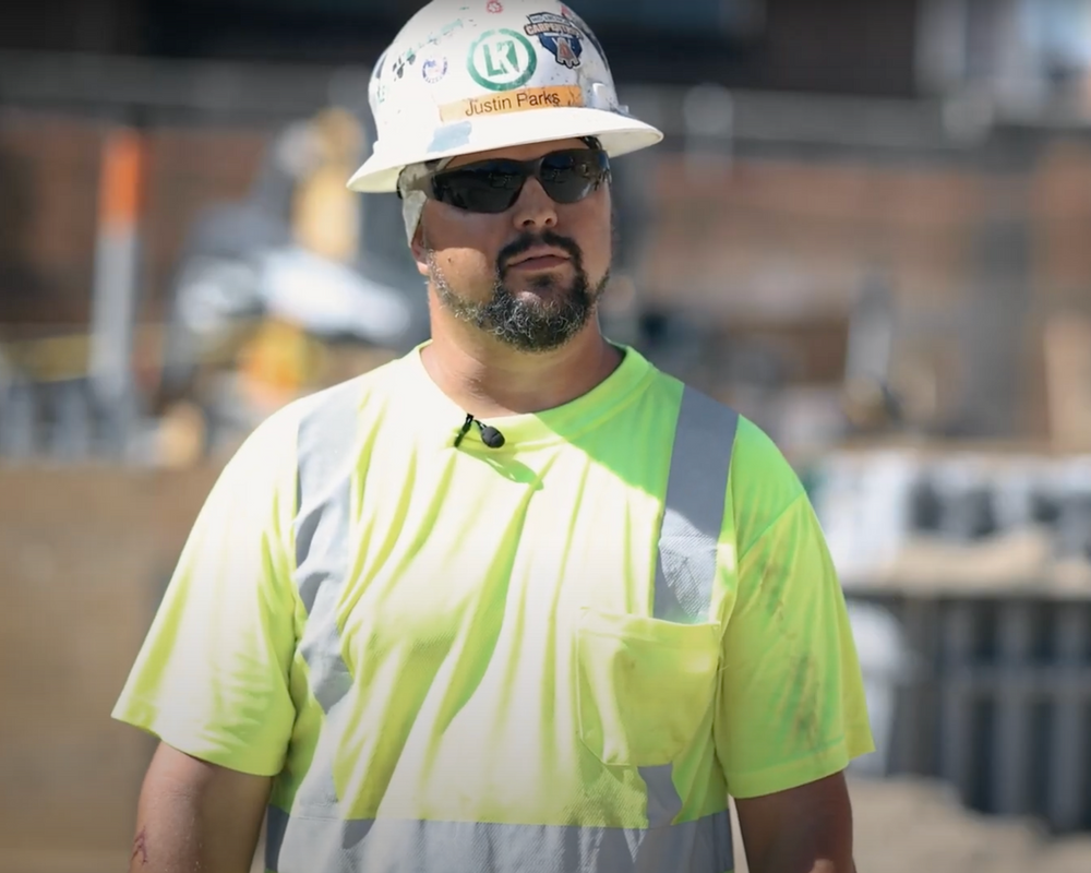 A man wearing a hard hat and sunglasses is standing on a construction site.