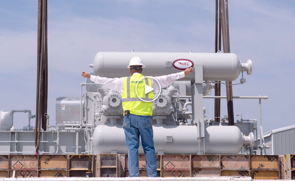 A man in a yellow vest and hard hat is standing in front of a large transformer.