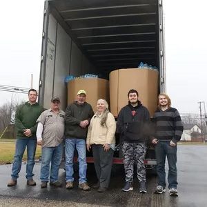 Six people standing at the back of an open truck loaded with large cardboard drums