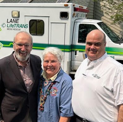 Three smiling people standing in front of a Lane LifeTrans ambulance.