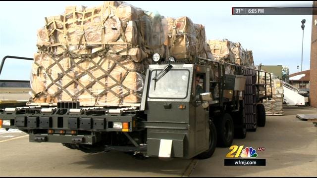 Military truck loaded with cargo crates on a road, viewed from the rear-left side.
