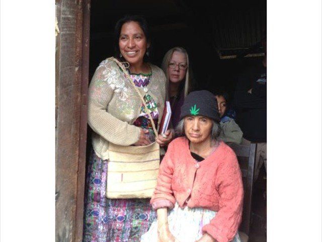 Two women standing in a doorway, one holding a bag and the other seated in a black hat and pink sweater.