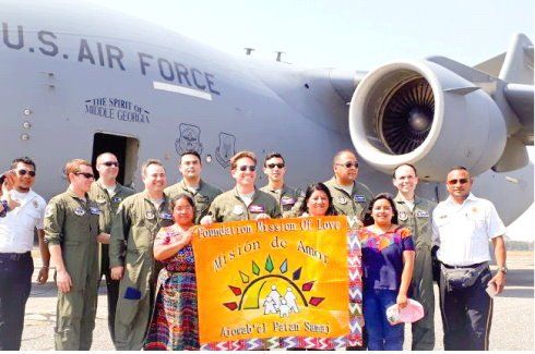 Group posing with orange banner in front of a U.S. Air Force aircraft, smiling at an airfield