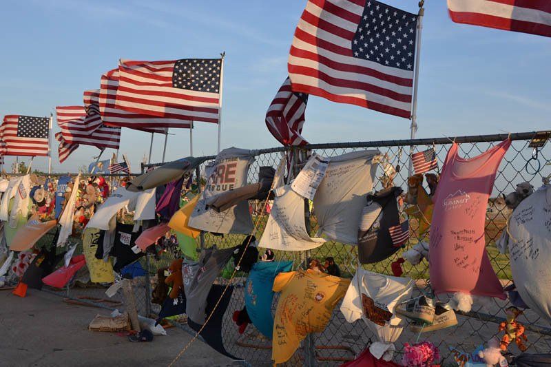 American flags and memorial notes tied to a roadside fence at sunset