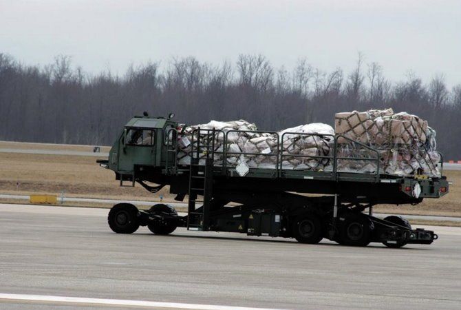 Military cargo truck on an airfield carrying a strapped-down load under a cloudy sky