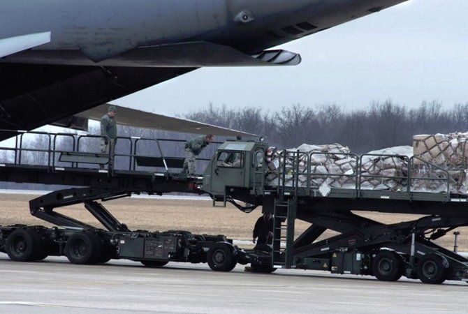 Military cargo truck loaded with supplies on an airport tarmac, partly under an aircraft wing