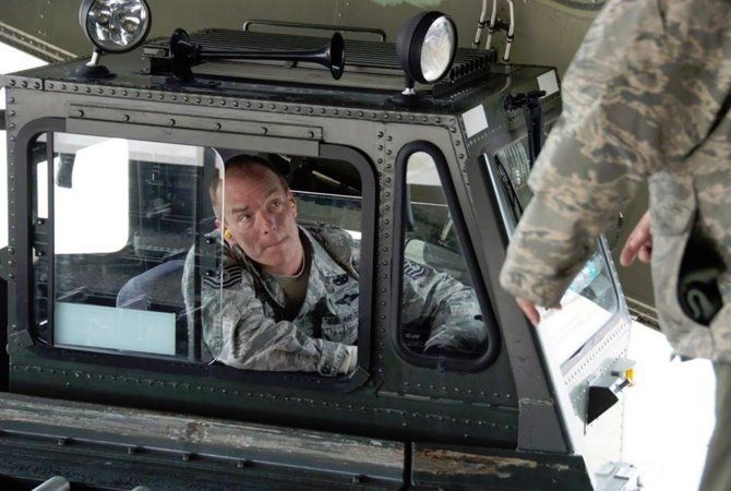 Person in camouflage inside a military vehicle, looking out through the window.