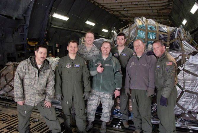 Six service members pose inside a cargo aircraft beside stacked pallets and netted freight.