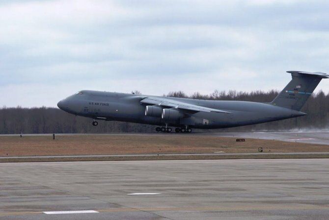 Large gray military cargo plane landing on a runway under an overcast sky