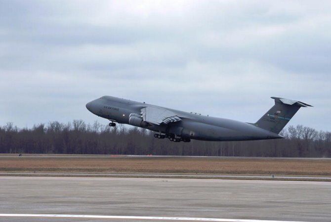 Gray military cargo plane taking off from a runway under a cloudy sky