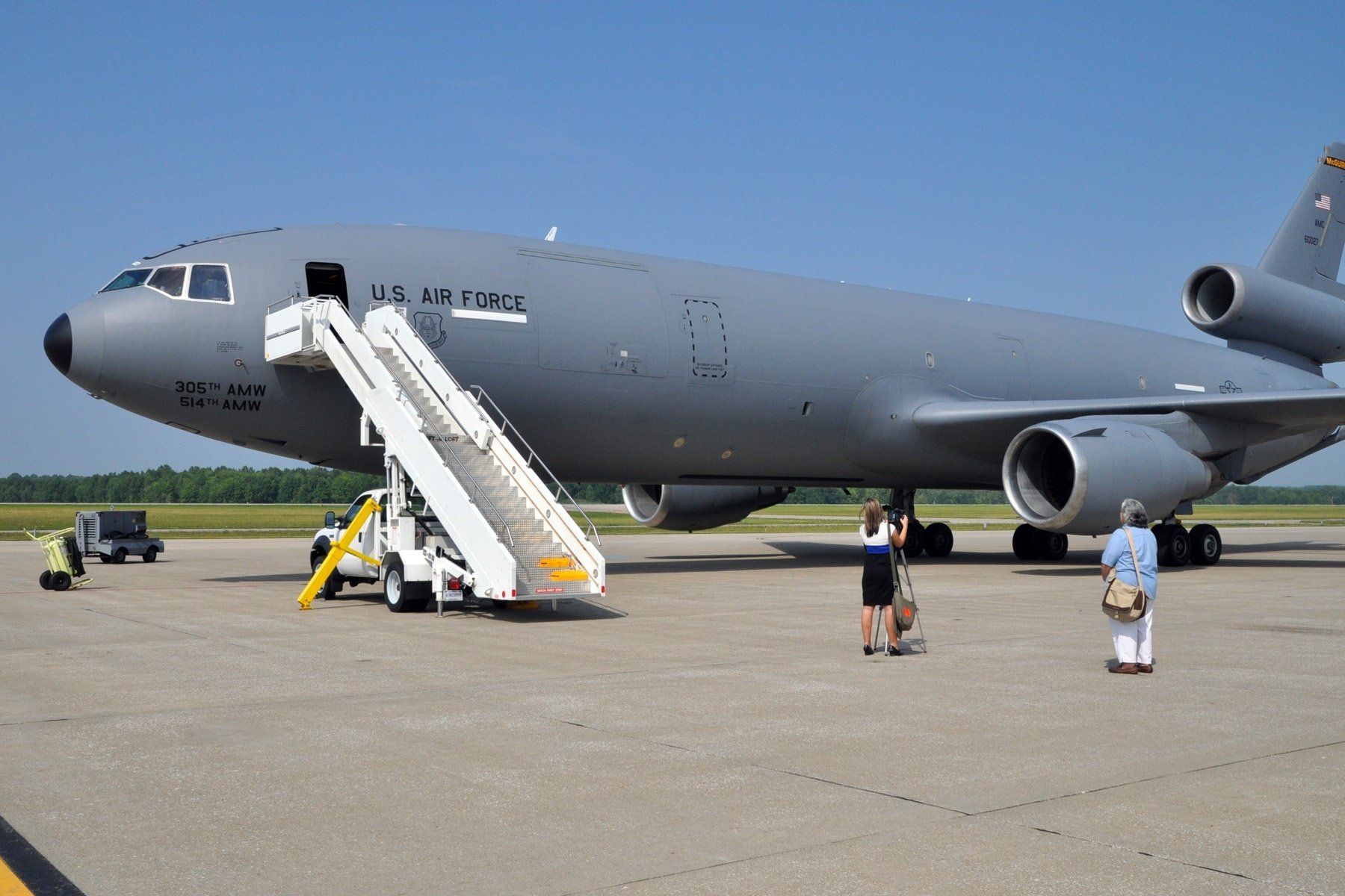 Gray military cargo plane on tarmac with stairs and a few people nearby