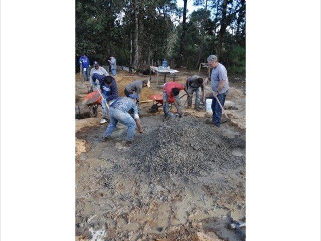 Workers shoveling wet concrete at an outdoor construction site near trees and mud.