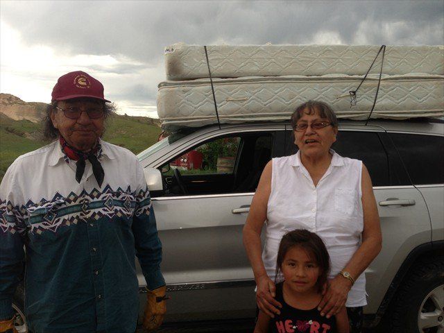 A man and two women standing next to a car with a mattress on top of it at Pine Ridge Reservation