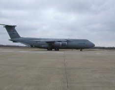 Gray military cargo plane parked on a runway under cloudy skies