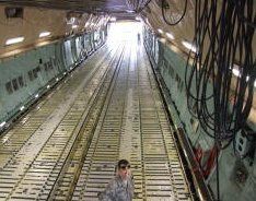 Steep aircraft cargo bay with rows of floor tracks and hanging cables, bright light at far end