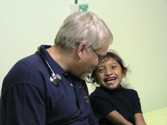 Older man in navy shirt smiling at a laughing child in a hospital hallway
