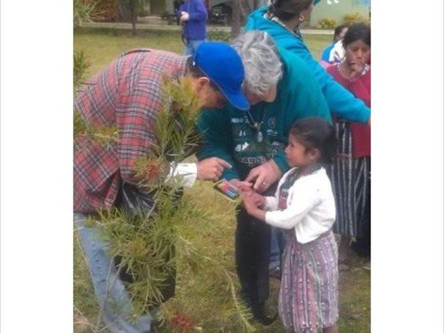 People planting a sapling together in a garden, with a child watching closely
