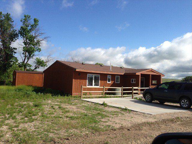Wooden house with a driveway, parked SUV, and cloudy blue sky