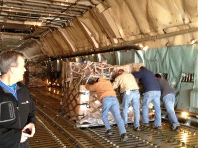 Workers unloading cargo inside a transport aircraft, pushing a pallet of goods toward the rear.