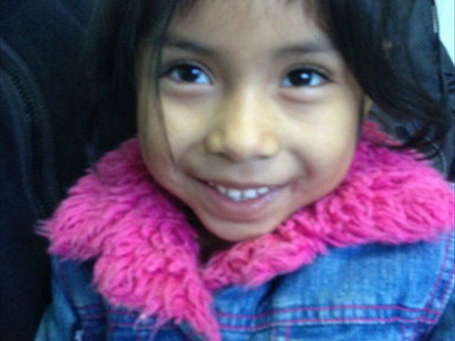 Close-up of a smiling child wearing a pink scarf and denim jacket