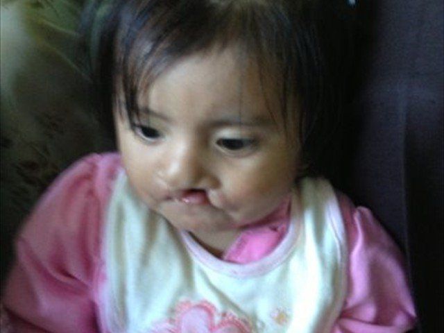 Young child in a pink shirt and white bib, looking down with a serious expression