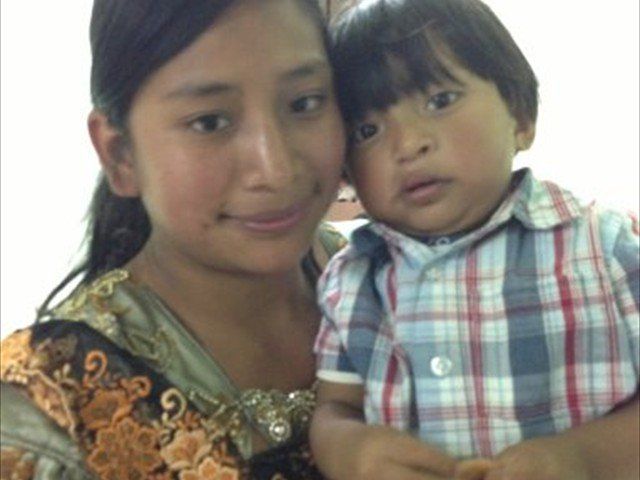 Woman holding a child, both looking at the camera, wearing patterned clothing.