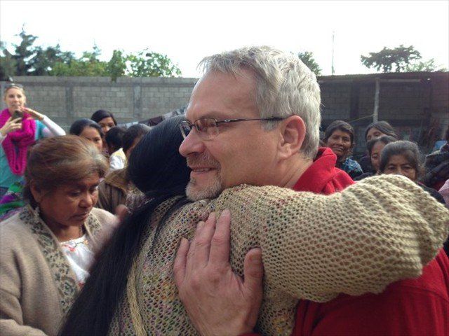 Two people hugging outdoors, with a crowd in the background.