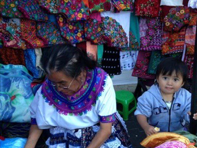 Vendor arranging colorful textiles beside a child sitting in a market stall
