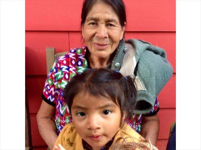 Two people in colorful clothing sit in front of a red wall, with a child in the foreground.