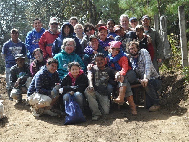 Group of people posing outdoors on a dirt path, with trees and rocks in the background.