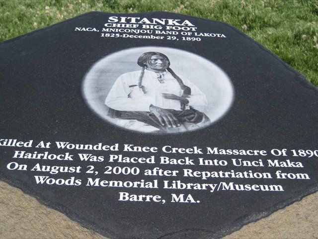 White memorial stone with Native figure and inscription honoring Sitting Bull at Wounded Knee Creek mass grave.