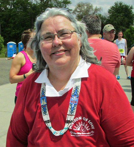 Smiling Kathleen Price in red shirt and lanyard at an outdoor event with other people in the background