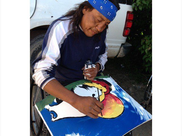 Person painting a colorful picture on a blue surface outdoors