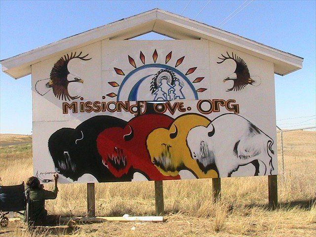 Mission of Love sign with painted buffalos in a dry field.