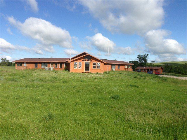 Single-story orange house in a grassy field under a blue sky with clouds.