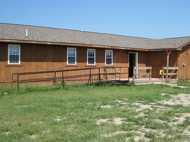Single-story brown building with ramp, windows, and grassy foreground under a blue sky