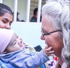 Close-up of a baby touching a woman's face, with a caregiver watching nearby.