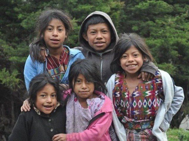 Five children in colorful jackets huddle together outdoors, smiling at the camera.