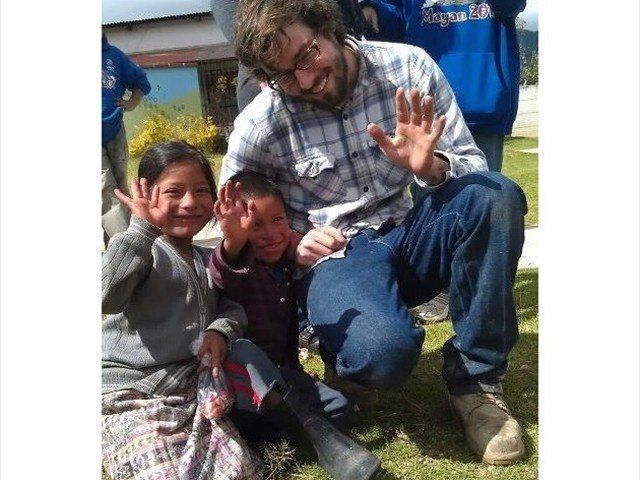 Three smiling children and an adult wave outdoors on grass.