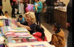 Children browsing colorful books at a library table with an adult nearby