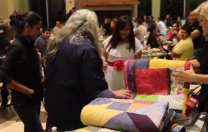 People gathered around colorful quilts on display at an indoor event.