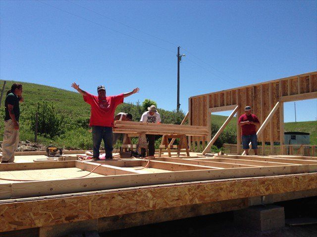 A man in a red shirt is holding a piece of wood at Pine Ridge Reservation