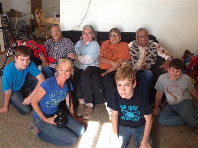 Group of people sitting on a couch and floor in a living room, smiling at the camera.