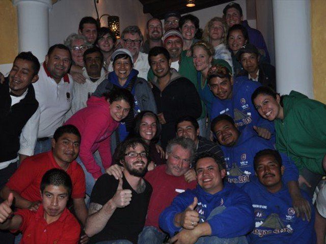 Large group of people posing indoors, smiling and giving thumbs up in a stairwell